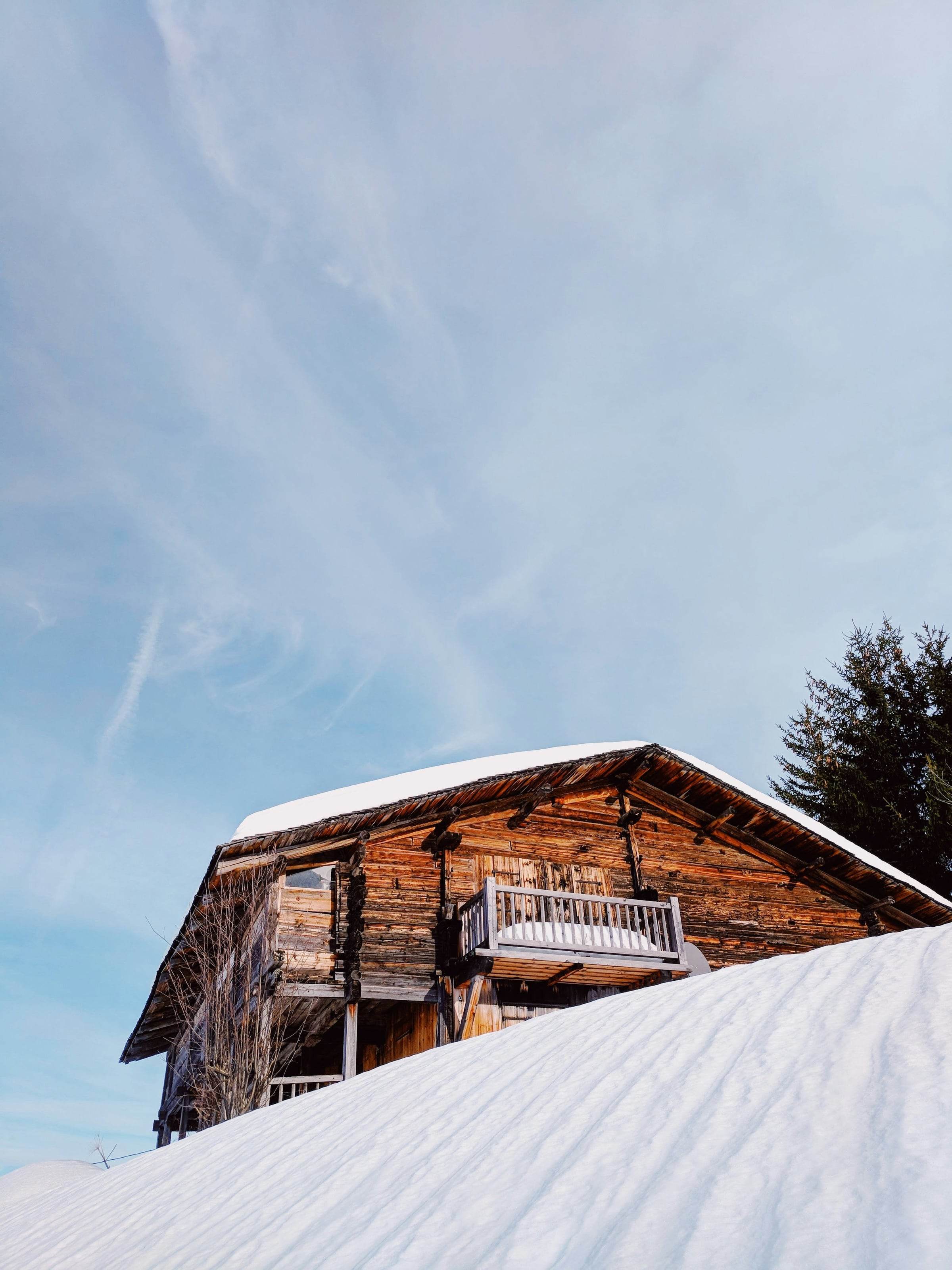 Chalet en madriers brunis et balcon de bois sur une pente enneigée, ciel d’hiver clair