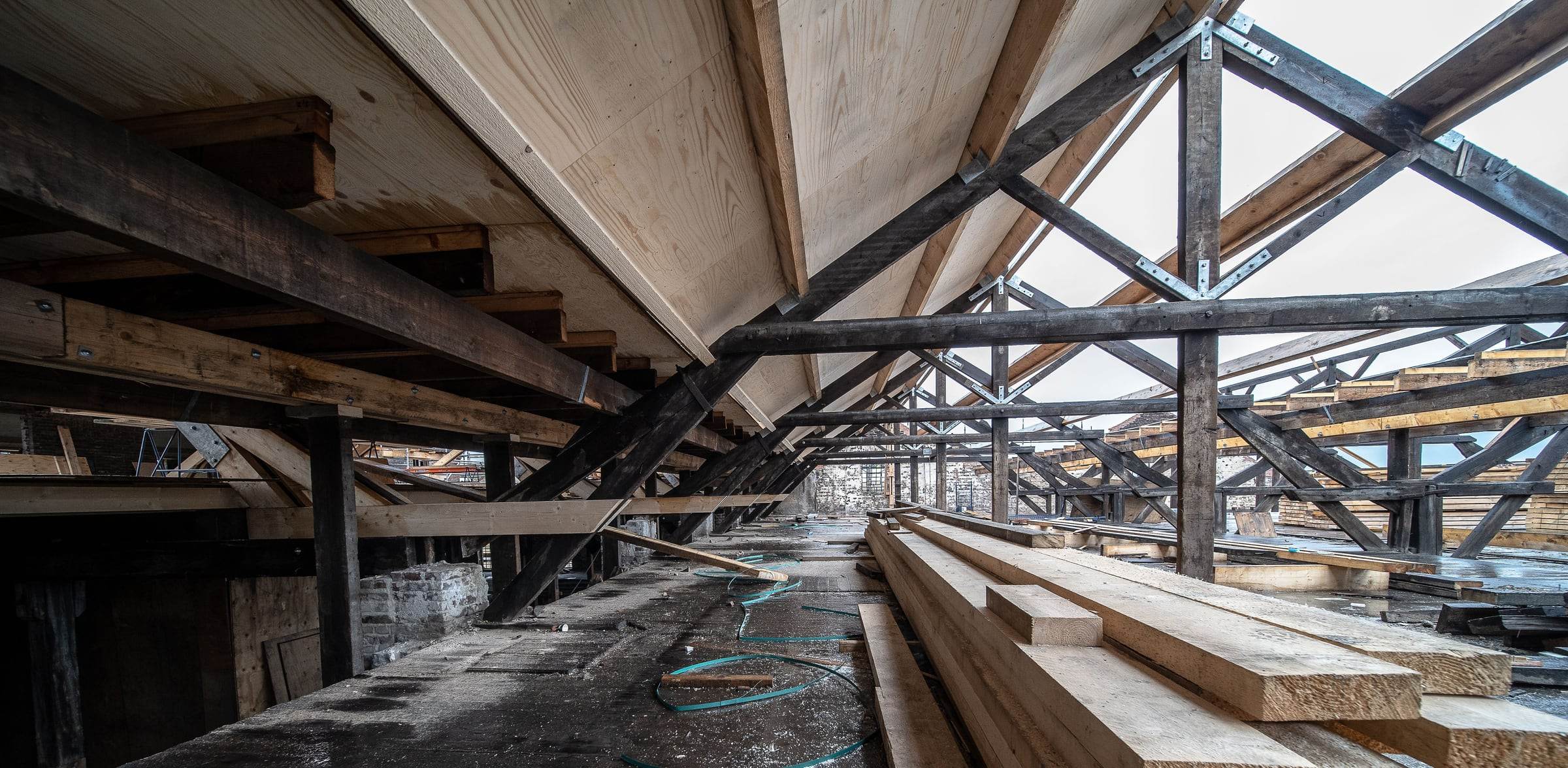 Charpente ancienne aux bois sombres, nouveaux panneaux de toiture en bois clair et planches neuves empilées sur le plancher du comble