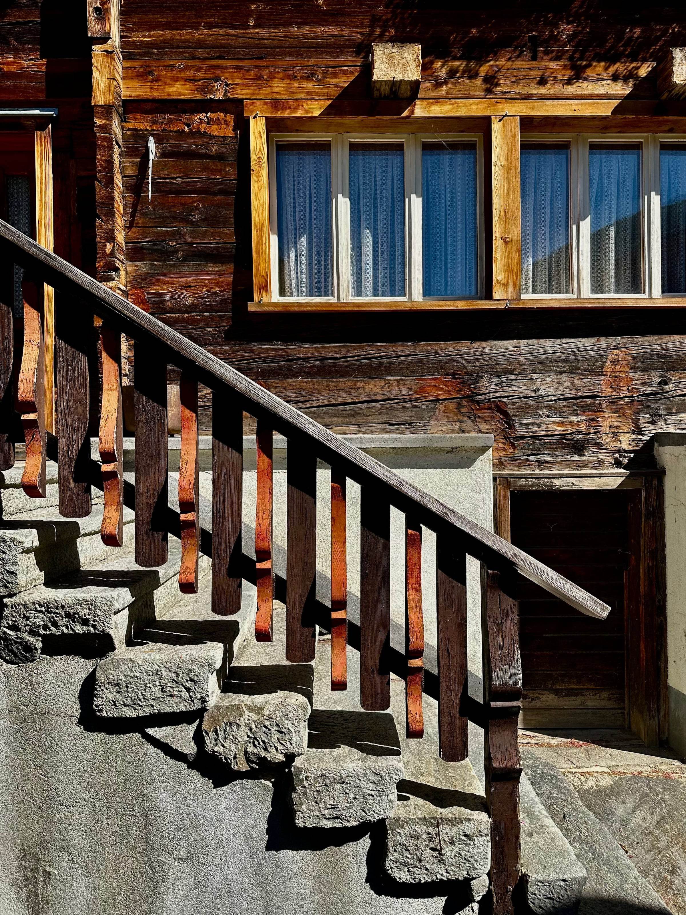 Escalier en dalles de pierre et garde-corps en bois devant une façade en madriers brunis
