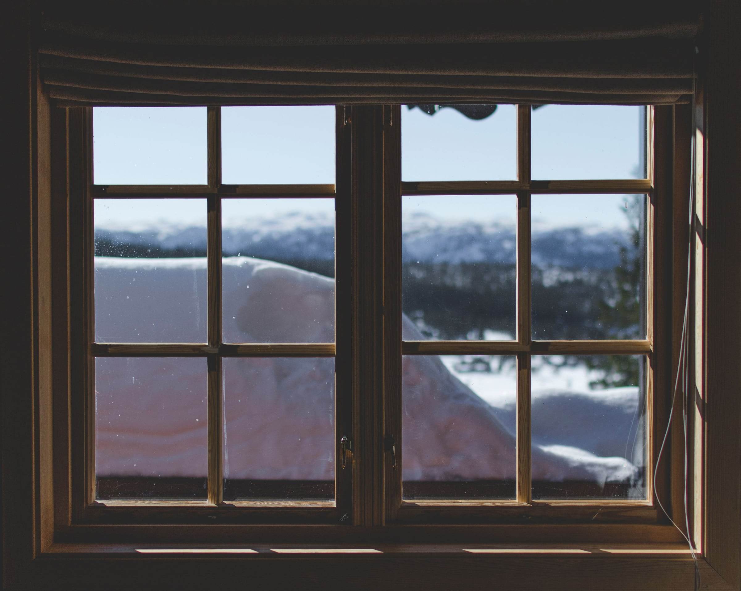 Double fenêtre en bois à petits bois vue de l’intérieur, neige et forêt de montagne derrière les carreaux