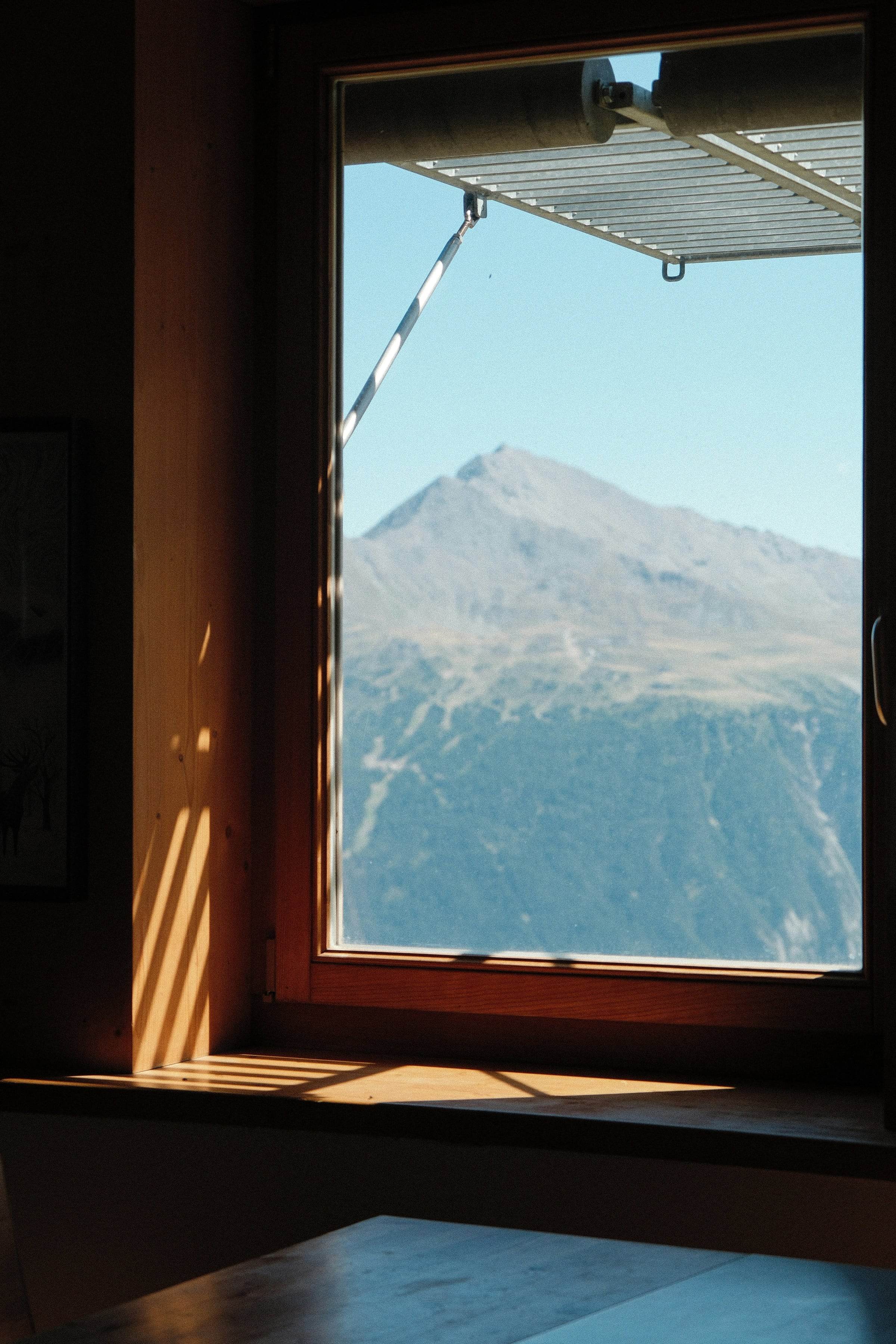 Fenêtre en bois dans un mur sombre, sommet de montagne et ciel clair dehors, ombres longues sur l’embrasure